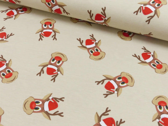 Reststück: Baumwolljersey Stoff kleines Rentier mit roter Nase und Weihnachtsmütze auf beigem Hintergrund; 0,5